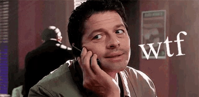 a man is talking on a cell phone in a room with a sign that says wtf .