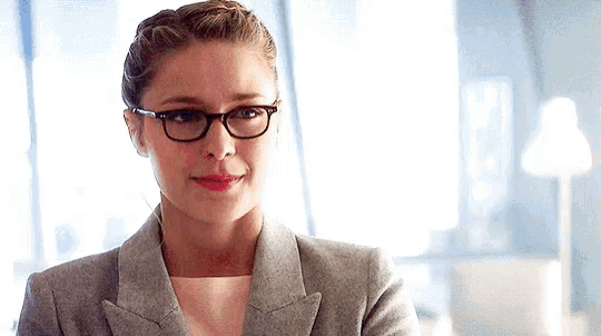 a woman wearing glasses and a gray jacket is looking at the camera .