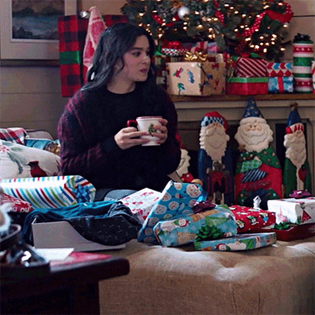 a woman is sitting on a couch surrounded by christmas presents and holding a cup of coffee .