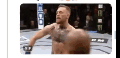 a man without a shirt is standing in a boxing ring with a gif button on the bottom right corner .