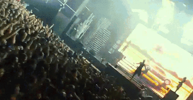 a crowd of people watching a concert with a large screen in the background