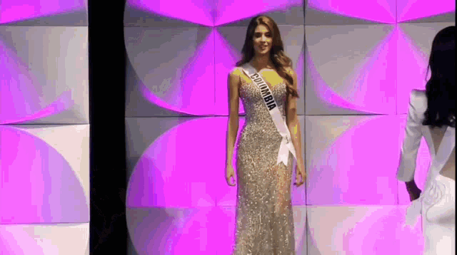 a woman wearing a sash that says columbia is walking on a stage .