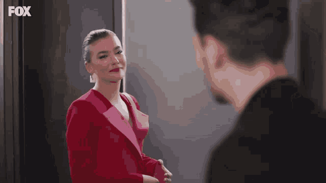 a woman in a red jacket is standing next to a man in a black shirt and looking at him .