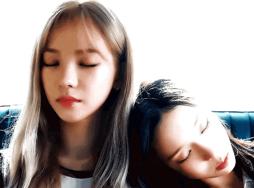 two girls are laying on a couch with their eyes closed .