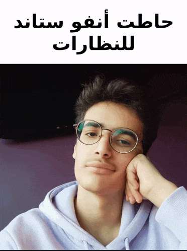 a young man wearing glasses and a purple hoodie with arabic writing on the bottom