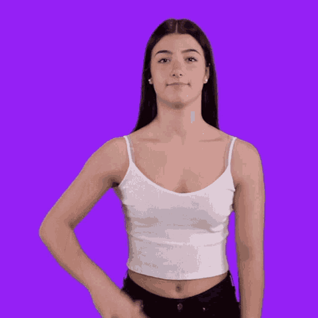a woman in a white tank top and black jeans is waving her hand in front of a purple background .