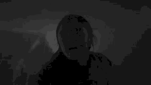 a black and white photo of a woman standing in the dark looking at the camera .