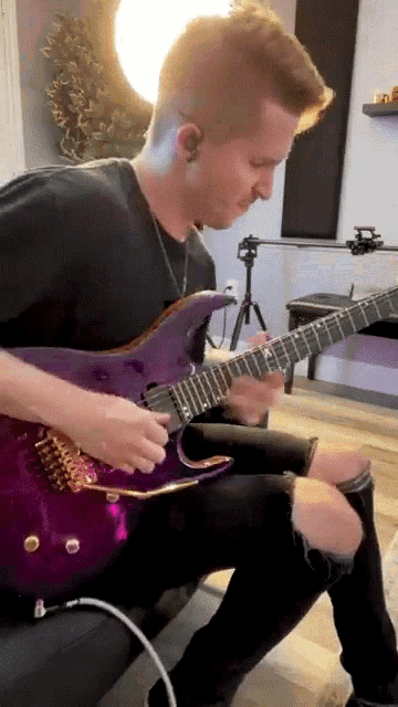 a man is playing a purple electric guitar in a room