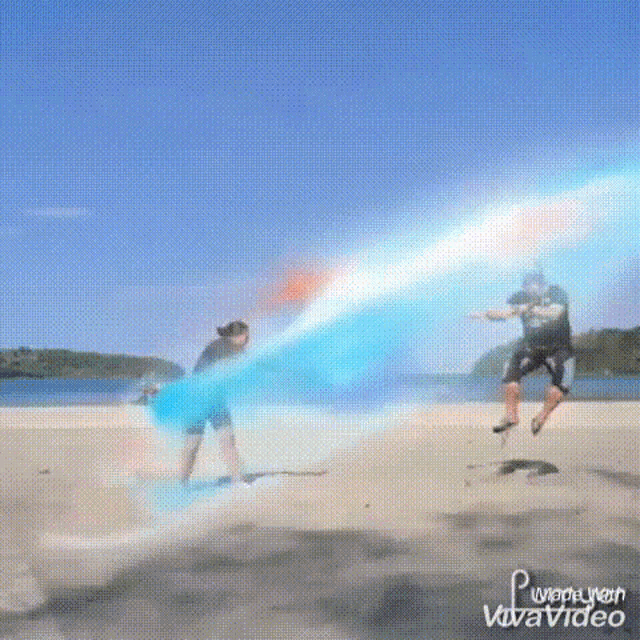 a man and a woman are jumping in the air on a beach with a blue beam coming out of their hands .