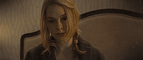 a woman is sitting on a bed in a dark room with her hair blowing in the wind .