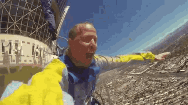 a man in a yellow jacket is flying through the air with his arms outstretched