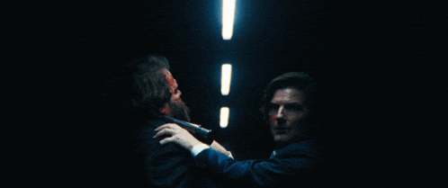 a man in a suit holds a gun over another man 's head