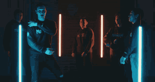 a man wearing a mu sweatshirt stands in a dark room with other men