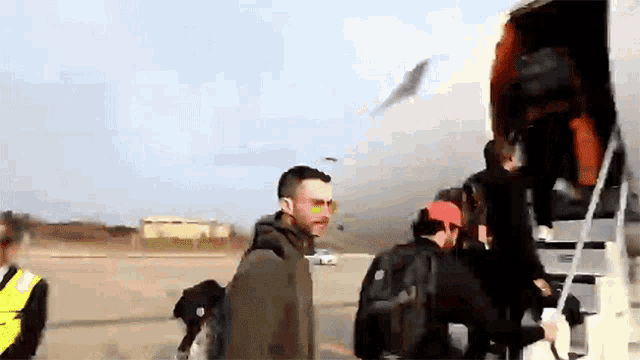 a group of people are boarding an airplane and one of them is wearing sunglasses and a backpack with the word north face on it