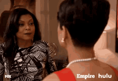 two women are standing next to each other and talking to each other in a living room .