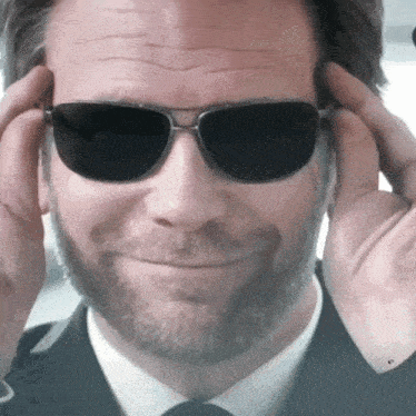 a man with a beard is wearing sunglasses and adjusting them