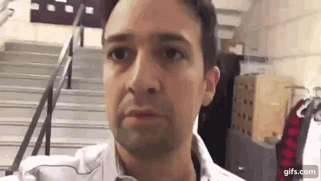 a man in a white shirt is standing in front of a set of stairs .