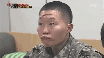 a soldier with a shaved head is making a funny face while sitting on a couch .
