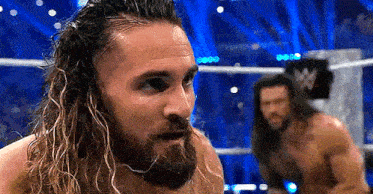a man with a beard and long hair is standing in a wrestling ring .