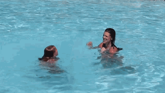 a woman is holding a child in a swimming pool while another woman watches .