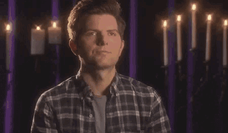 a man in a plaid shirt is standing in front of a wall with candles .