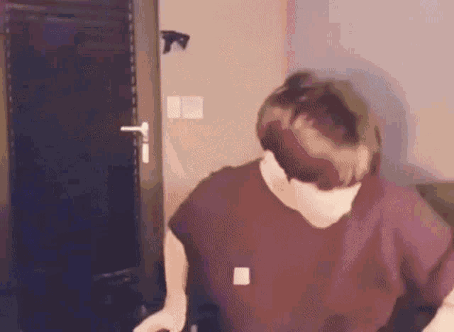 a man in a purple shirt is standing in front of a door in a dark room .