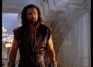 a man with long hair and a beard is standing in a room with a sword in his hand .