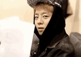 a young man wearing a hat and a hooded jacket is sitting on a couch .