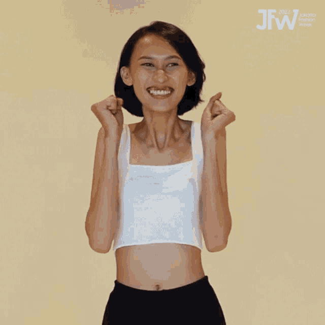 a woman wearing a white crop top and black shorts is smiling and holding her fists up in the air