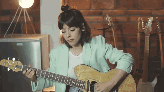 a woman is playing a guitar in front of a brick wall