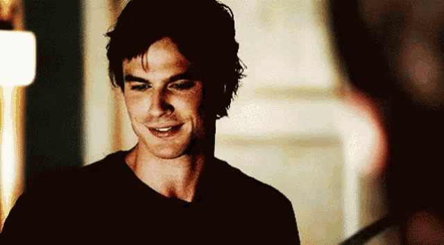 a man in a black shirt smiles while standing in a dark room