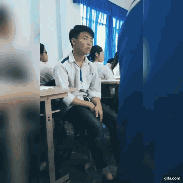 a boy sits at a desk in a classroom with a gifs.com watermark