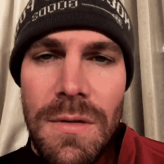 a close up of a man with a beard wearing a beanie and making a funny face .