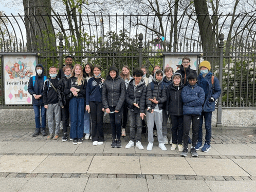 a group of young people are posing for a picture in front of a fence with a sign that says toria hof