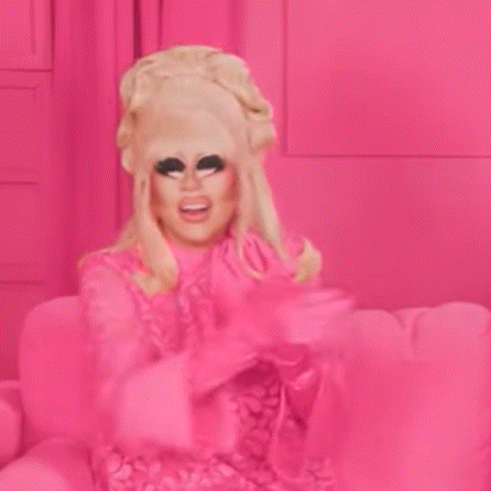 a drag queen is sitting on a pink couch wearing a pink dress and fur coat .
