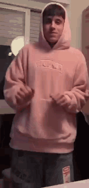 a young man wearing a pink hoodie and shorts is standing in a room .