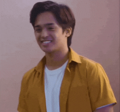 a young man in a yellow shirt is smiling and looking at the camera .