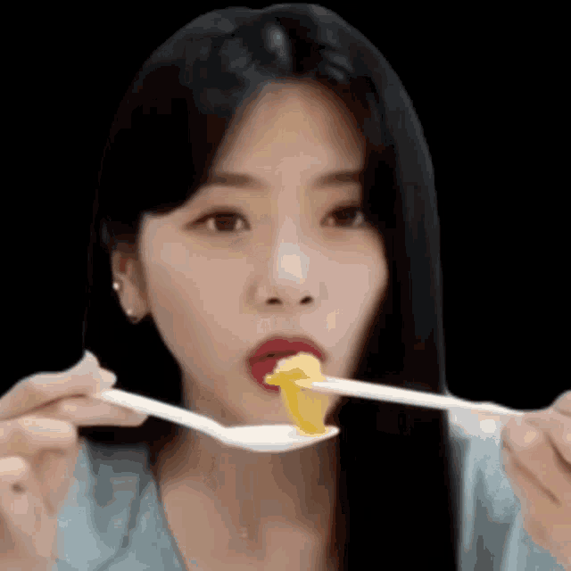 a woman is eating a piece of food with a spoon and chopsticks .