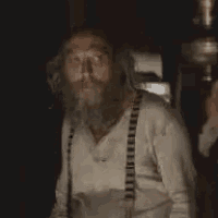 a man with a beard and suspenders is giving a thumbs up sign .