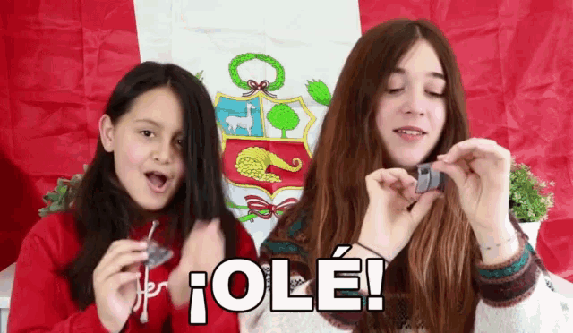 two girls are holding objects in front of a peruvian flag and one of them is saying ole