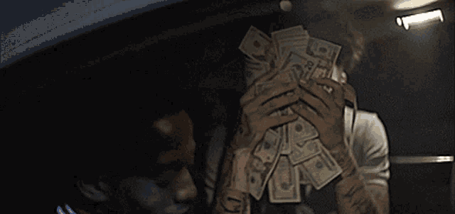 a man is holding a pile of money in front of his face that has the number 10 on it