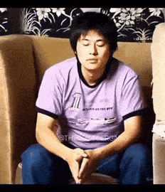 a man in a purple shirt with the number 1 on it sits on a couch