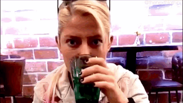 a woman is drinking a green drink from a glass while sitting at a table .