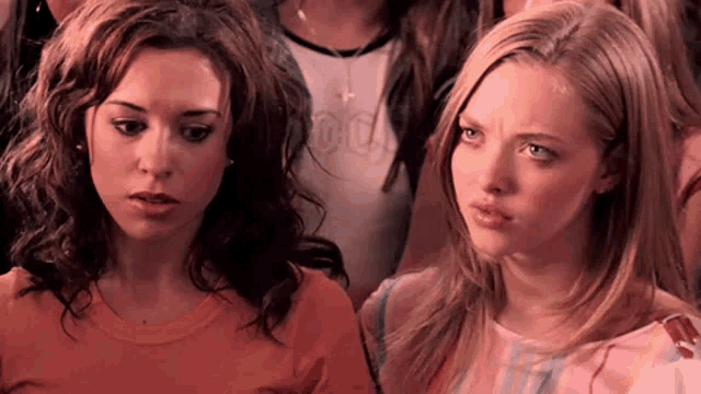 two women are sitting next to each other in a crowd of people and making funny faces .