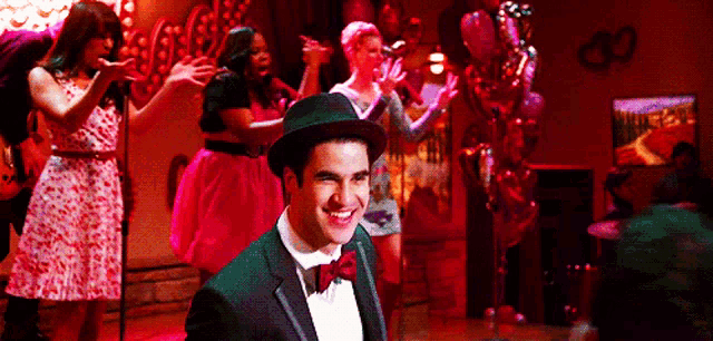 a man in a tuxedo and bow tie is smiling in front of a group of people