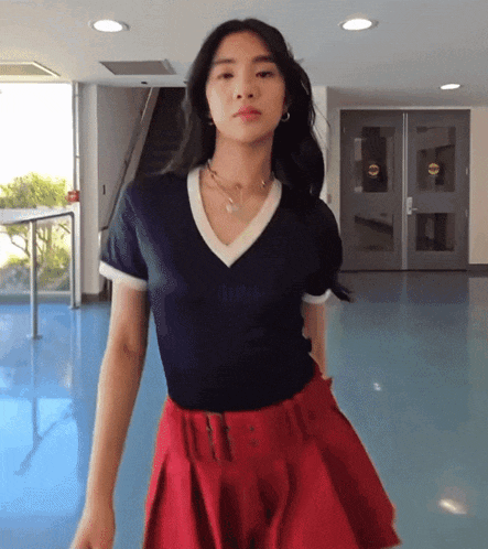 a woman wearing a red skirt and a black top stands in front of a door that says ' emergency exit ' on it