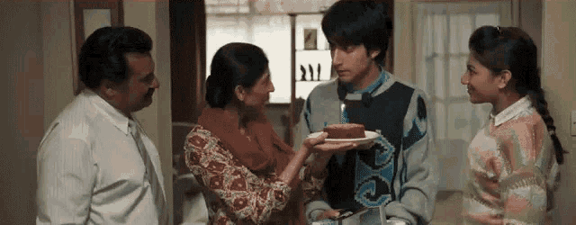 a group of people are standing around a table with a man holding a cake .