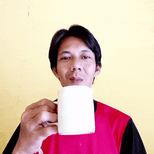 a man wearing a red and black shirt is drinking from a white mug