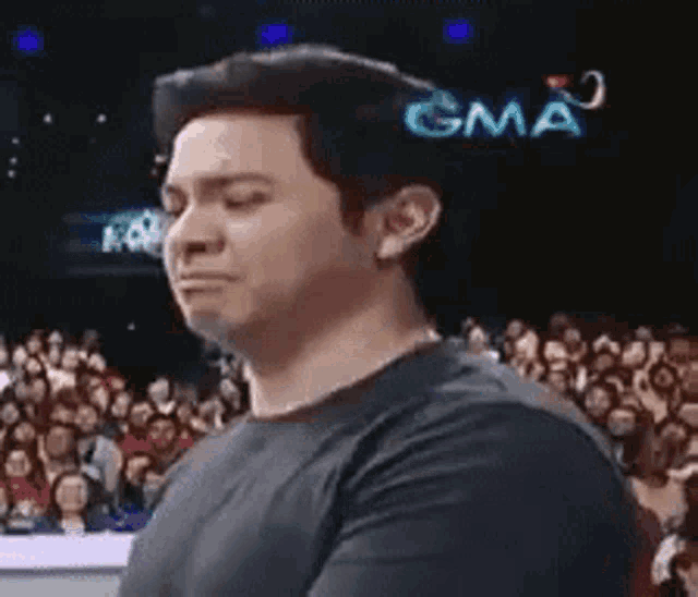 a man in a black shirt is standing in front of a crowd of people and making a funny face .