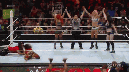 a group of women are standing in a wrestling ring with a referee